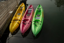 Brightly Colored, Yellow, Pink & Green Kayaks Docked & Sitting On Still Waters, Reflecting The Back Ground.