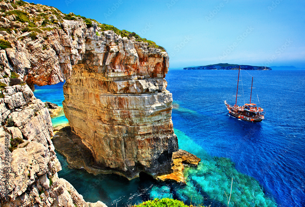 Tourist boat passing next to Trypitos (also known as "Kamara"), a natural rocky arch at Paxos island, Ionian Sea, GREECE. In the background, Antipaxos island. - obrazy, fototapety, plakaty 