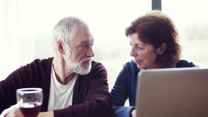 Poster - A portrait of senior couple with wine indoors at home, using laptop.
