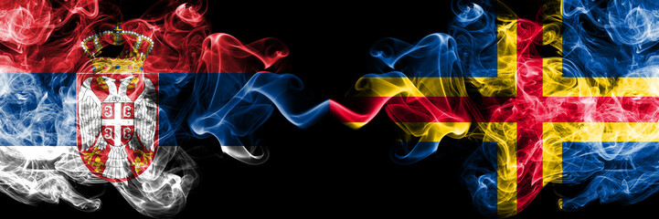 Serbia vs Aland smoky mystic flags placed side by side. Thick colored silky smokes combination of Serbian and Aland flag