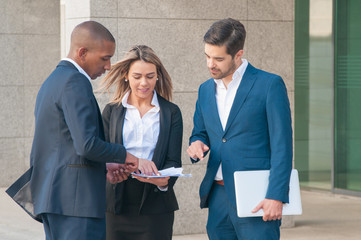 Smiling young businesswoman showing papers to male colleagues. Multiethnic business team discussing documents outdoors. Discussion concept