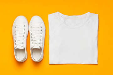 White female fashion sneakers, white T-shirt on yellow orange background. Flat lay top view copy space. Women's shoes. Stylish white sneakers. Fashion blog or magazine concept. Shoe background, sport