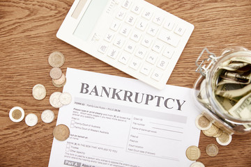 Wall Mural - top view of bankruptcy form, coins, calculator and glass jar with dollar banknotes on wooden table