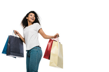 happy curly african american girl holding shopping bags isolated on white