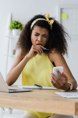 Wall Mural - selective focus of exhausted african american woman yawning and covering face while looking at smartphone