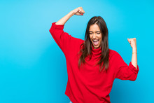 Young Woman With Red Sweater Over Isolated Blue Background Celebrating A Victory