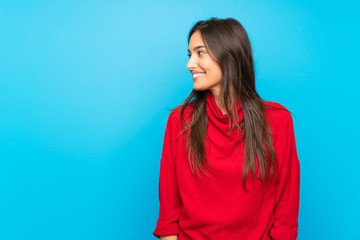 Young woman with red sweater over isolated blue background looking to the side