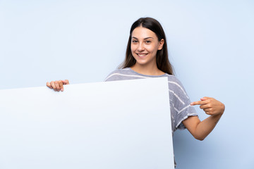 Young brunette woman over isolated blue background holding an empty white placard for insert a concept