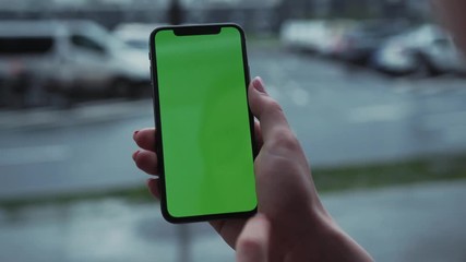 Los Angeles, California - 5 April 2019: Close up view woman hands use holding vertically smart phone cellphone with green screen background rain parking cars weather app outside rain trees raindrops