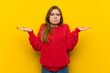 © luismolinero - Young woman over yellow wall having doubts while raising hands