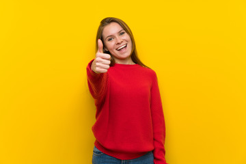 Young woman over yellow wall with thumbs up because something good has happened