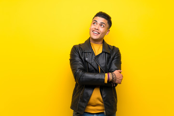 Young man over isolated yellow background looking up while smiling