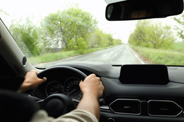 Wall Mural - Man driving car on rainy day, closeup of hands