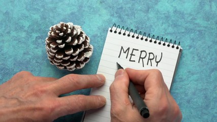 Canvas Print - merry xmas, greeting card - man hand writing a note with a black marker in a spiral notebook, overhe