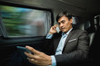 © Odua Images - busy asian businessman calling by phone and using tablet on his way to meeting while sitting on passenger seat of his car