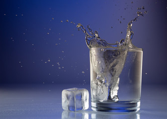 Wall Mural - Pouring water into glass on blue background close up