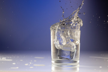 Wall Mural - Pouring water into glass on blue background close up