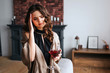 © estradaanton - Young businesswoman work at home. Stand in living room with glass of red wine in hand. Headache. Alone. Wear black dress and brown shawl.