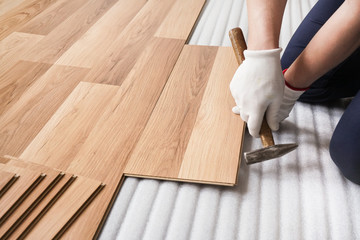 Wall Mural - Installing laminated floor, detail on man hands fixing one tile with hammer, over white foam base layer