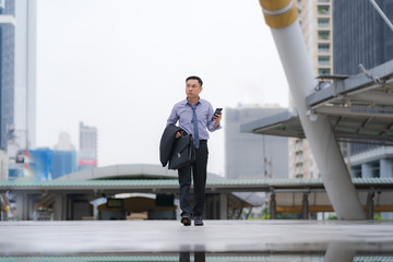 Wall Mural - Asian Businessman walking and holding briefcase with business office buildings in the city background