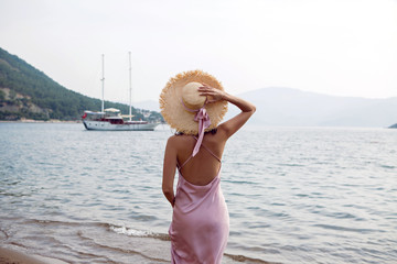 girl in straw hat and pink dress walking on the beach