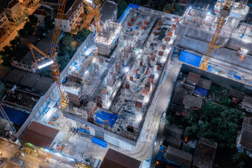 Aerial view of busy industrial construction site workers with cranes working. Top view of development high rise architecture building at night.