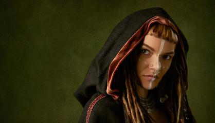 Wall Mural - Beautiful, young, stylish woman in a black, tribal hood on green background