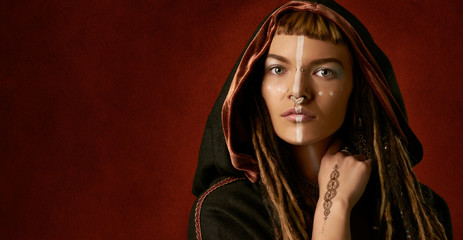 Wall Mural - Beautiful, young, stylish woman with dreadlocks in a black, tribal costume on red background