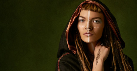 Wall Mural - Beautiful, young, stylish woman with dreadlocks in a black, tribal costume on green background