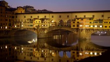 Ponte Vecchio Bridge, Florence, Italy. Evening Yellow-colored Bridge Reflecting In Arno River. Panoramic Shot, 4K