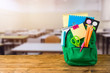 Back to school concept with bag backpack and school supplies on wooden table over classroom background