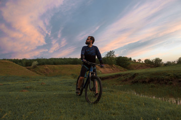 Cyclist in shorts and jersey on a modern carbon hardtail bike with an air suspension fork rides off-road on the orange-red hills at sunset evening in summer	