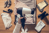 Top view on the woman holds hair dryer packing clothes in the open suitcase. Travel concep