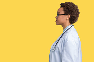 Wall Mural - Young african american doctor woman wearing medical coat over isolated background looking to side, relax profile pose with natural face with confident smile.