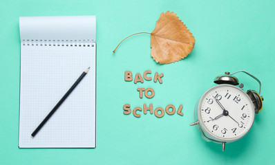 School time minimal concept. Notepad, pencil, alarm clock on blue background with slogan back to school from wooden letters. Top view