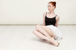 © oleg_ermak - Nice redheaded ballerina sits on the white wood floor She wears a light dance wear and a peach tutu. Copy space