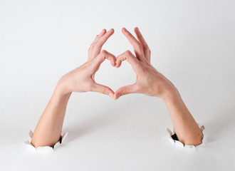 Wall Mural - Female hands show a heart symbol through the torn holes of a white background. Creative art