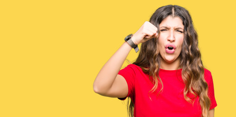 Sticker - Young beautiful woman wearing casual t-shirt angry and mad raising fist frustrated and furious while shouting with anger. Rage and aggressive concept.