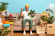 © WHstudio Leushin N - Shot of overjoyed guy clenches fist, poses at sofa, holds wrapped houseplant, moves in new modern house, being estate owner, has to unpack personal stuff from boxes. Home, tenant, relocation concept
