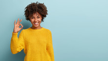 Okay, Its Fine. Charming Good Looking Young Afro Woman Says No Problem, Shows Excellent Gesture, Has Tender Smile, Gives Recommendation, Demonstrates Positive Approval, Dressed In Yellow Sweater