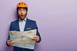 © wayhome.studio  - Elegant male builder tries find office, being on way to job interview, holds paper map, shocked choosing wrong route, wears helmet, formal apparel, focused aside, isolated on purple studio wall