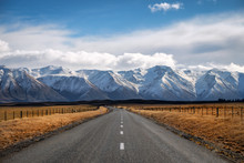 A Long Straight Road Path Journey Towards Snow Mountains In New Zealand.