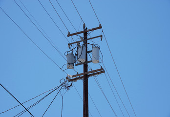 Electricity distribution pole with wiring cables and electrical equipment seen against a bright blue sky