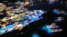 Aerial Drone Night Shot Of Famous Psarou Beach With Luxury Resorts And Yachts Docked, Mykonos Island, Cyclades, Greece