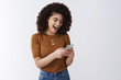 © Cookie Studio - So awesome simple. Cheerful attractive young relaxed curly dark hair stylish girl laughing open mouth excited reading daring message hold smartphone reacting amused funny video online look display