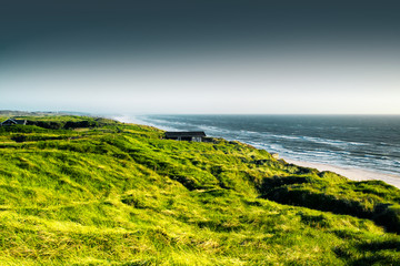 beautiful bright green coastline sand dunes with grass and a typical danish vacation house with nort