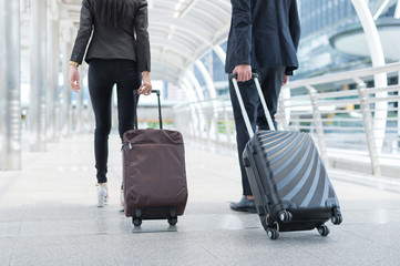 Wall Mural - back of businessman and businesswoman walk together with luggage on the public street, business travel and trip concept