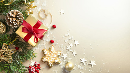 Wall Mural - christmas light gold background with beautiful golden gift box with red ribbon, fir branches, cones,