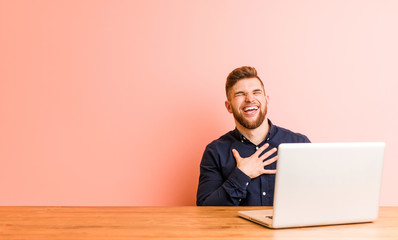 young man working with his laptop laughs out loudly keeping hand on chest.