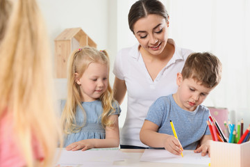 little children with kindergarten teacher drawing at table indoors. learning and playing